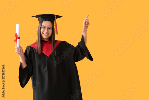 Young female graduate with diploma on yellow background