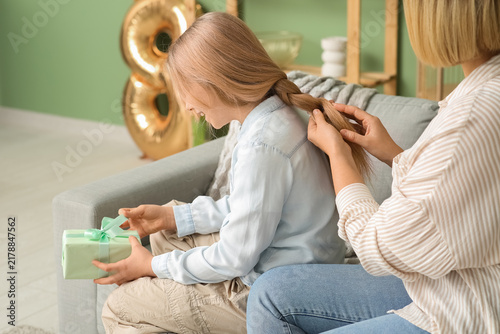 Beautiful young woman doing hair her cute little daughter with gift box and s...