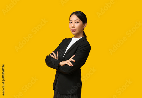 Portrait of confident Asian businesswoman with crossed arms on yellow background