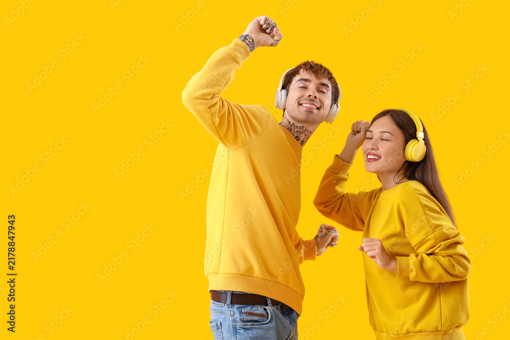 Obraz premium Young couple in headphones dancing on yellow background