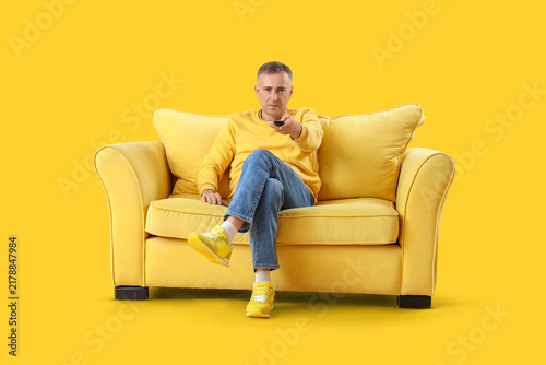 Mature man on sofa watching TV against yellow background