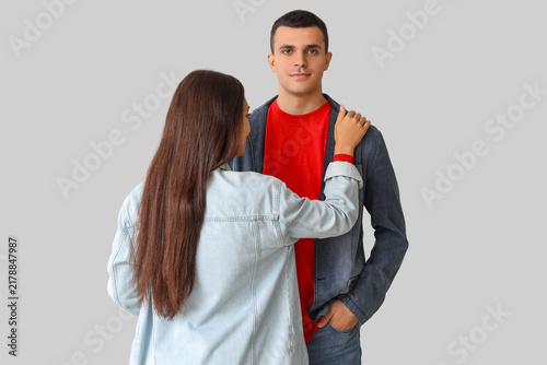 Stylish young couple in denim jackets hugging on light background