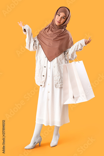 Beautiful Muslim woman with shopping bags on yellow background