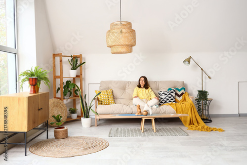 Pretty young woman sitting on white sofa in light living room