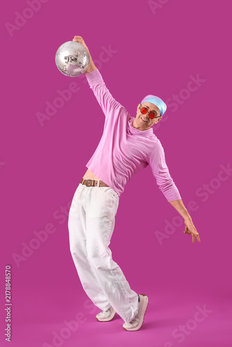 Cool mature man with disco ball dancing on purple background