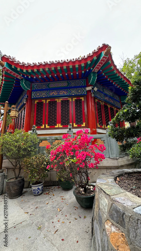 serene outdoor garden area with a static chinese-style pavilion and flowers in pots, surrounded by stone walls and trees, featuring concrete and wood materials.