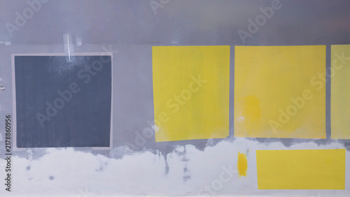Close-up of yellow and grey paint test squares on an outdoor building wall. Exterior wall restoration process with colorful paint swatches on plaster.