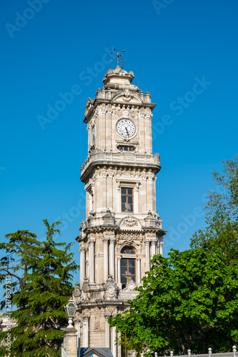Clock tower with ornate design and white fence in sunny park setting