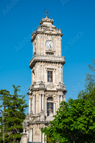 Clock tower with ornate design and white fence in sunny park setting