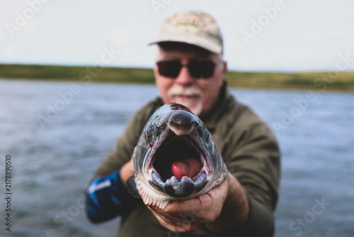 Angler proudly holds freshly caught salmon toward camera, mouth open to reveal vivid detail of fish and lure, capturing Alaska’s fishing excitement and success.