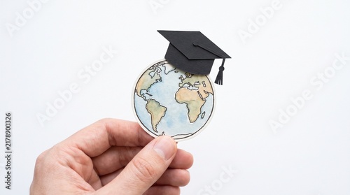 Hand holding a cutout of the Earth wearing a graduation cap symbolizing global education and academic achievement