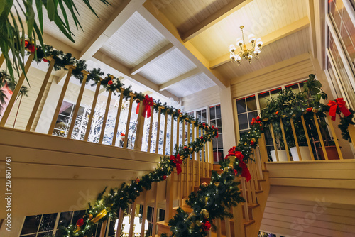 Fotografie Festive Staircase Elegance: A grand staircase adorned with vibrant Christmas garlands, twinkling lights, and festive red bows evokes a warm and inviting holiday spirit