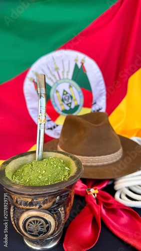 Chimarrão, gaucho hat and scarf on the table, and the flag of the state of Rio Grande do Sul - Brazil  in the background. Farroupilha Week.