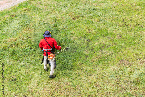 Worker trimming overgrown grass in urban park