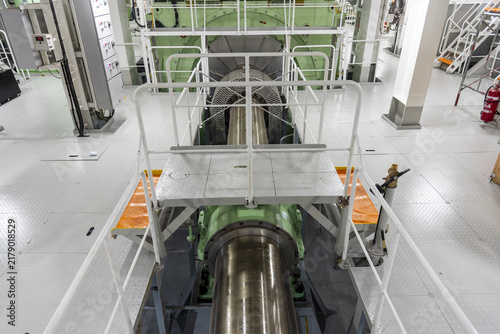Interior view of a large commercial vessel's engine room looking along the propulsion shaft toward the main engine, with the lower machinery space and shaft generator visible.