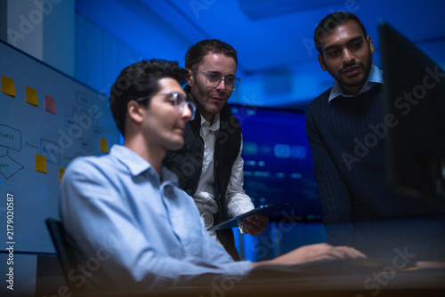 Bild auf Leinwand A seated analyst and two standing colleagues watching the same screen lean towar