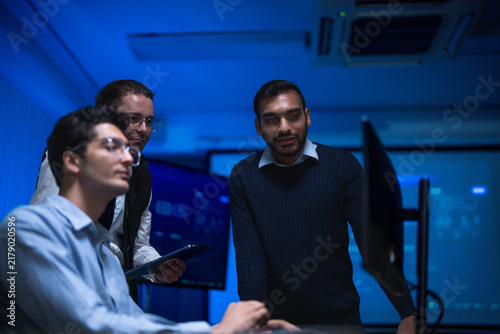 Bild auf Leinwand A seated analyst and two standing colleagues watching the same screen lean towar