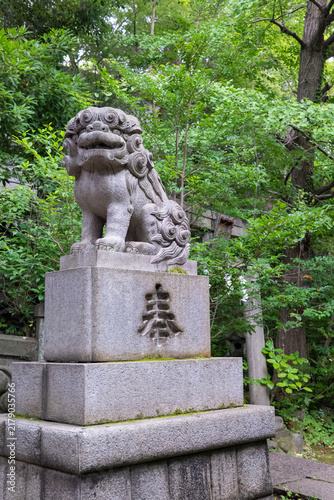 Fotografie Stone Guardian Lion Statue surrounded Green Leaves at Japanese shinto shrine