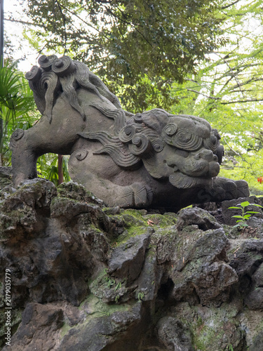 Foto Stone Guardian Lion Statue surrounded Green Leaves at Japanese shinto shrine