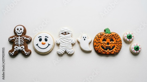 A collection of hand-decorated Halloween cookies shaped like a skeleton, a spooky ghost, a wrapped mummy, a carved pumpkin, a smiling face, and pair of creepy eyeballs