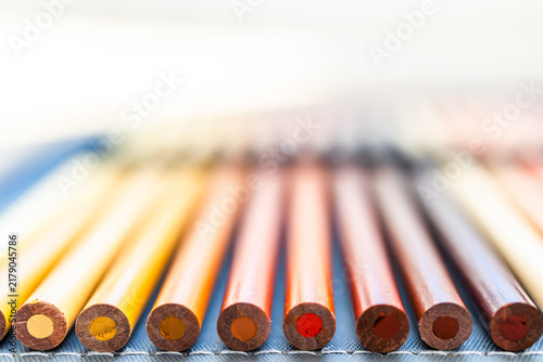 close-up of yellow orange and red colored pencils neatly lined up in pencil case, bottom of the pencil in focus