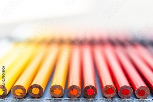 close-up of yellow orange and red colored pencils neatly lined up in pencil case, bottom of the pencil in focus