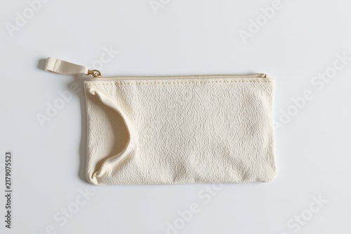 A minimalist beige fabric pouch with a zipper and wrist strap lies flat on a light surface, showcasing a simple and functional design.