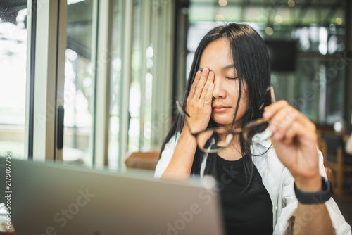 Tired woman removing glasses and rubbing her eyes while working on a laptop, illustrating eye strain, visual fatigue, prolonged screen time, stress and digital work.
