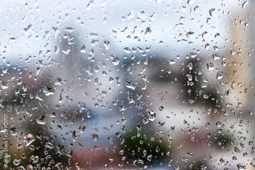 Close-up of water drops on a glass window pane during a rainy day in Brazil, creating a textured surface with a colorful soft blurred city background.