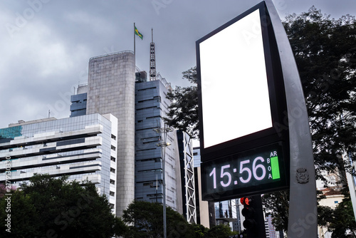 Digital billboard with blank white mockup display on Paulista Avenue. A modern street clock with an isolated white screen frame for advertisement placement, 