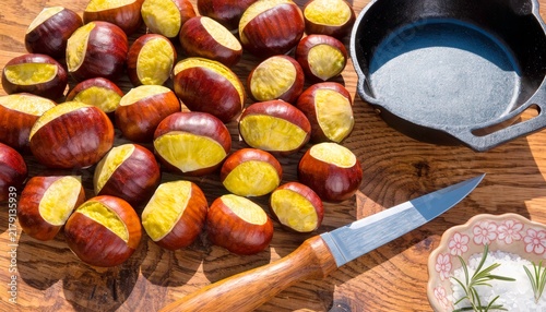 Chestnuts cut and ready for cooking on a wooden table with a cast iron pan