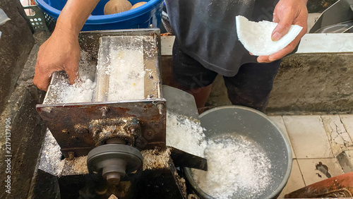 Foto A vendor using an electric coconut grating machine to grate fresh white coconut meat into fine flakes at a local traditional market stall