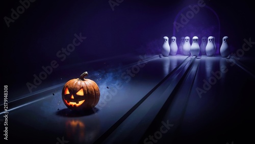 Jack o lantern pumpkin rolls down bowling lane towards ghost pins for spooky halloween party game and fun.