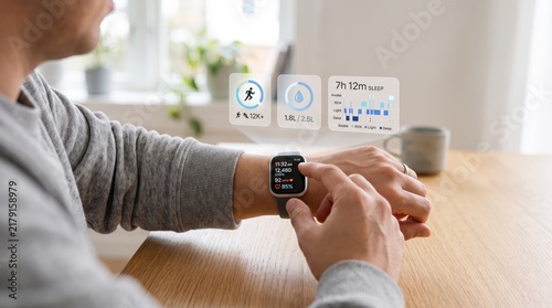 Man using smartwatch with futuristic hologram interface displaying health metrics, sleep tracking data, and fitness statistics in modern home office environment, digital wellness