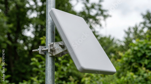 White panel antenna mounted on metal pole against green trees. Wireless telecommunication equipment for 5g network signal