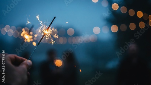 Person holding a glowing sparkler at festive outdoor celebration