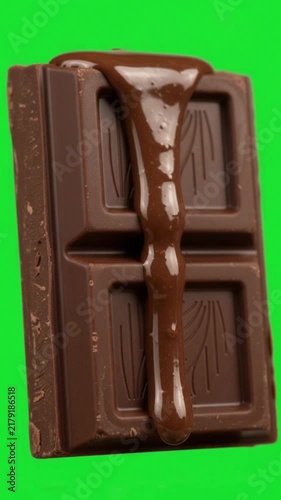 Liquid chocolate dripping over chocolate bar on green screen background