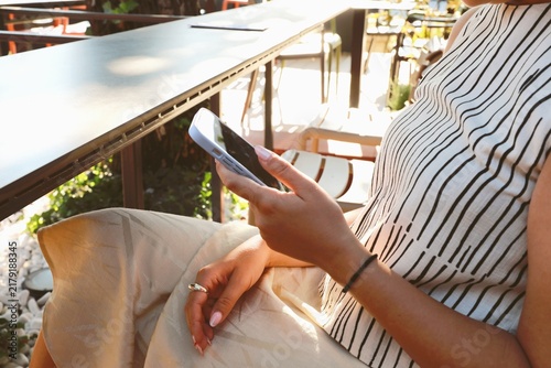 Woman Relaxingat at an outdoor cafe Using  a Smartphone on a sunny day.