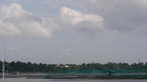 Time-lapse of moving thick clouds over a series of floating fish cages or aquaculture pens deployed on a lake, along with small wooden caretaker huts