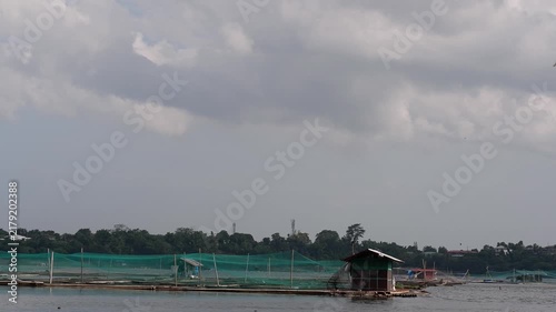 Time-lapse of moving thick clouds over a series of floating fish cages or aquaculture pens deployed on a lake, along with small wooden caretaker huts