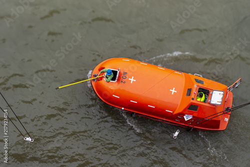 Fotografie Rescue boat seen from above while maneuvering alongside a commercial vessel after a simulated emergency alarm, preparing for connection to the recovery system