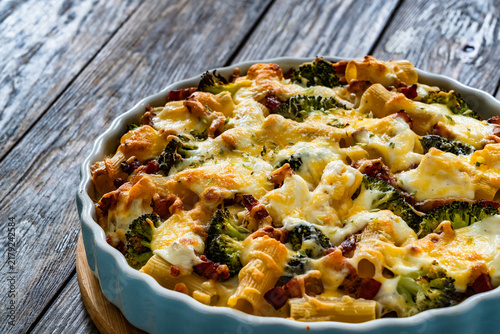 Pasta casserole with broccoli and smoked bacon on wooden table

