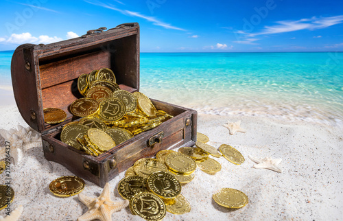 Foto Treasure chest on a white sand beach with gold coins.
