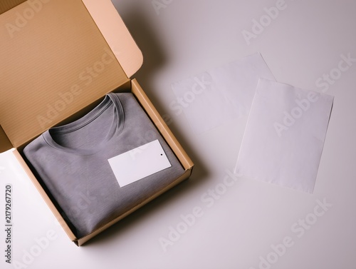 Minimal clothing packaging with a blank shirt label, tissue paper, and cardboard box