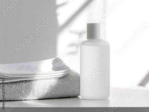 Minimal white skincare bottle with folded towels and soft natural light in a clean bathroom setting