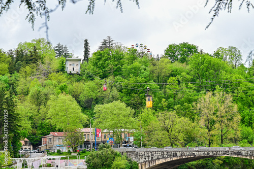 Historic cable car with a red cabin crossing a river bridge in the valley of the mining town of Chiatura, Imereti region, Georgia