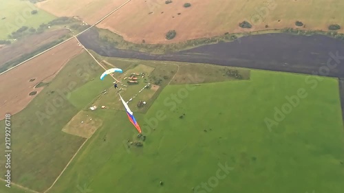 An aerial view of two parachutists over fields and an airfield. One athlete is descending with a large Russian tricolor.
