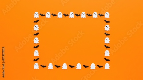 A festive halloween frame made of small white ghost figures and black bats on a vibrant orange background