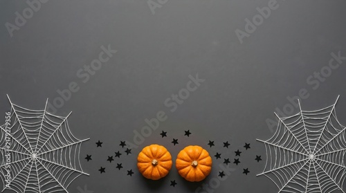Two small orange pumpkins surrounded by spider webs and black confetti on a dark grey background