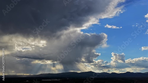A 4k drone timelapse of sun rays breaking through clouds over a dark silhouetted mountain range, highlighting dramatic weather and shifting climate dynamics in the Southwest sky.